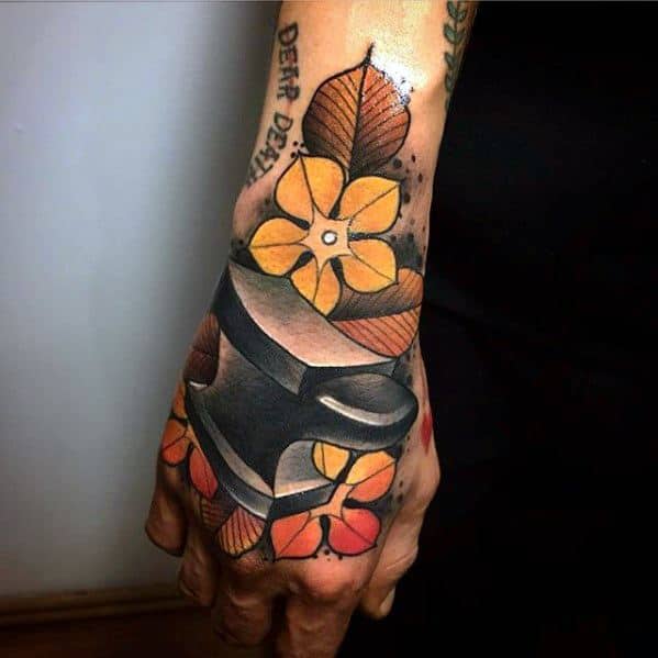Colorful anvil tattoo on the hand surrounded by bold yellow, orange, and red flowers with brown leaves, blending traditional and floral styles.