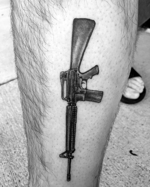 Black and grey AR-15 tattoo on the leg, featuring detailed shading and a classic rifle design, symbolizing strength, precision, and firearm appreciation.