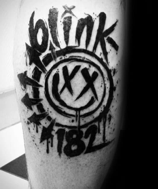 Black and white tattoo of the Blink-182 smiley face logo with the band name "BLINK" in graffiti-style lettering, accompanied by the number "182" and dripping ink effects, creating a bold and edgy design.