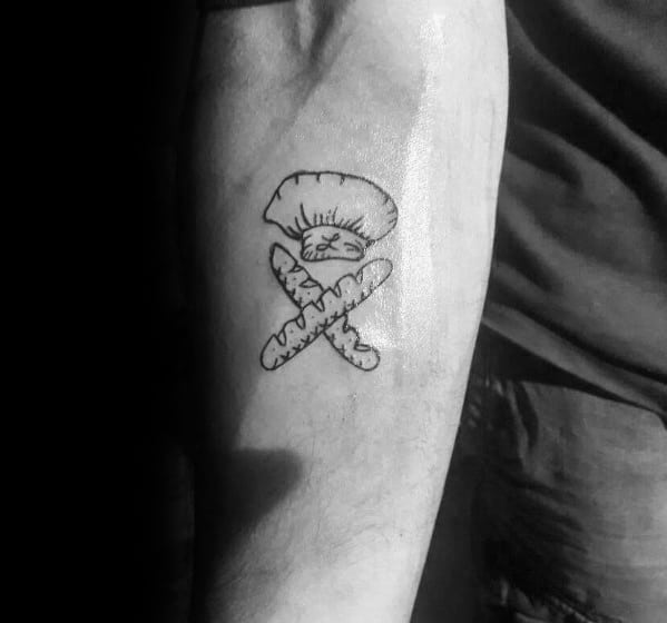 Simple black ink tattoo of a chef's hat above two crossed baguettes, creating a minimal yet symbolic design representing baking and culinary passion.