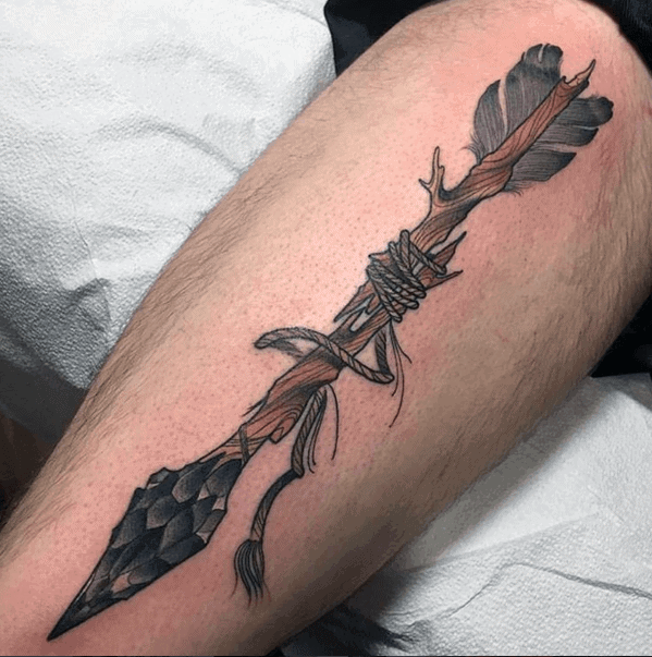 Highly detailed broken arrow tattoo featuring a stone tip, wrapped twine, and a natural wood shaft with jagged edges and feathered fletching.