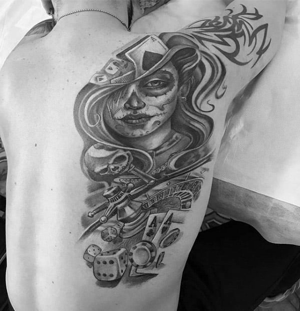 La Catrina back tattoo of a woman with sugar skull makeup and a fedora, surrounded by a skull, guns, dice, cards, and graffiti lettering.