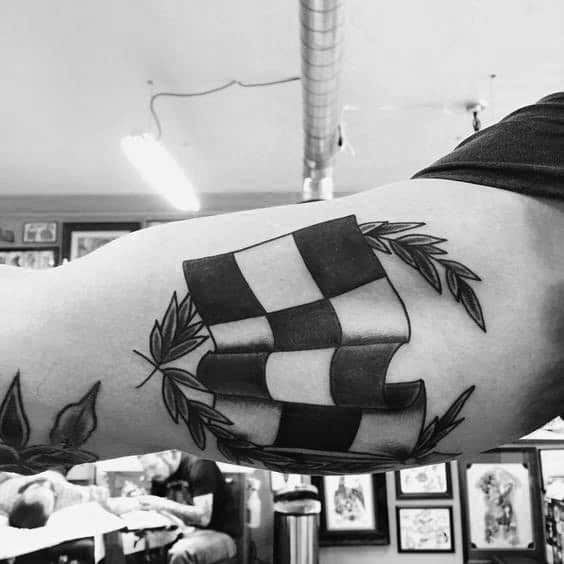 Bold checkered flag tattoo with a laurel wreath, symbolizing victory, racing achievement, and competitive spirit.