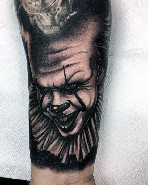 Black and grey tattoo of Pennywise with a sinister grin, sharp eyes, and detailed shading, capturing the eerie essence of the horror icon.