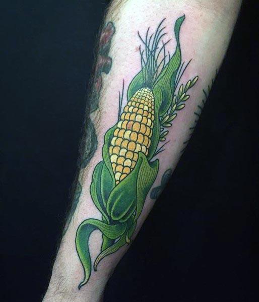 Bold tattoo of a detailed corn cob with vibrant green husks and golden kernels, wrapped with wheat stalks for a natural look.