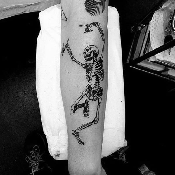 Bold dancing skeleton tattoo with raised arms and dynamic movement, inked in black for a striking and energetic design on the leg.