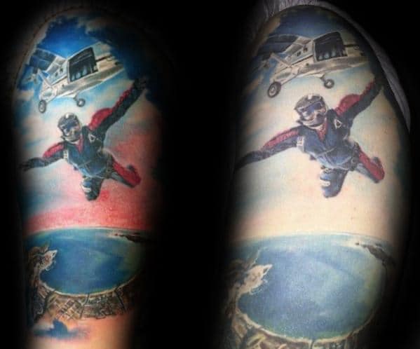 Colorful tattoo of a skydiver mid-fall with a plane above and coastal scenery below, capturing the thrill of freefall on the upper arm.