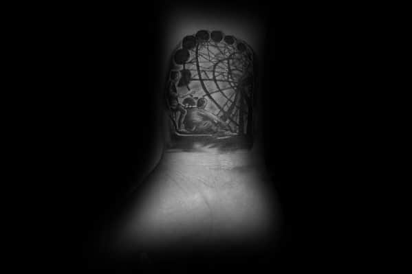 Dark-themed Ferris wheel tattoo on the wrist, featuring detailed shading and a surreal perspective, creating a moody and mysterious atmosphere.
