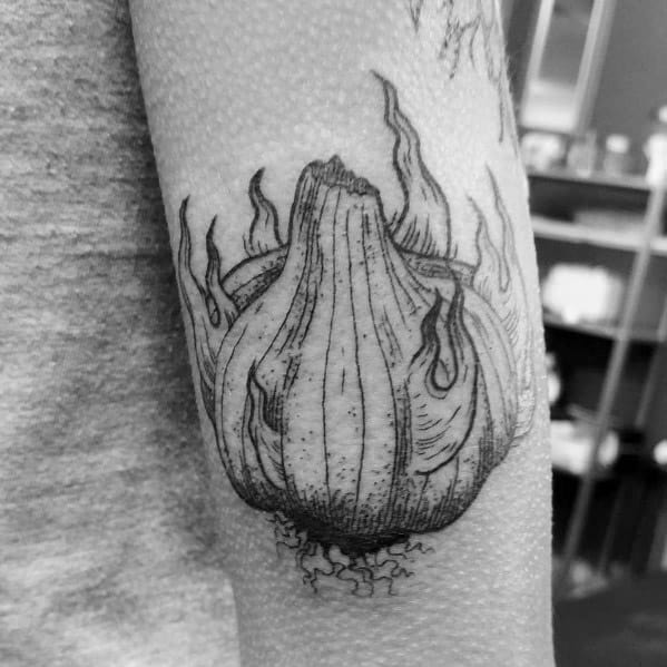 Black and grey garlic tattoo with fine line shading and flame-like details, creating a bold and unique botanical design on the forearm.
