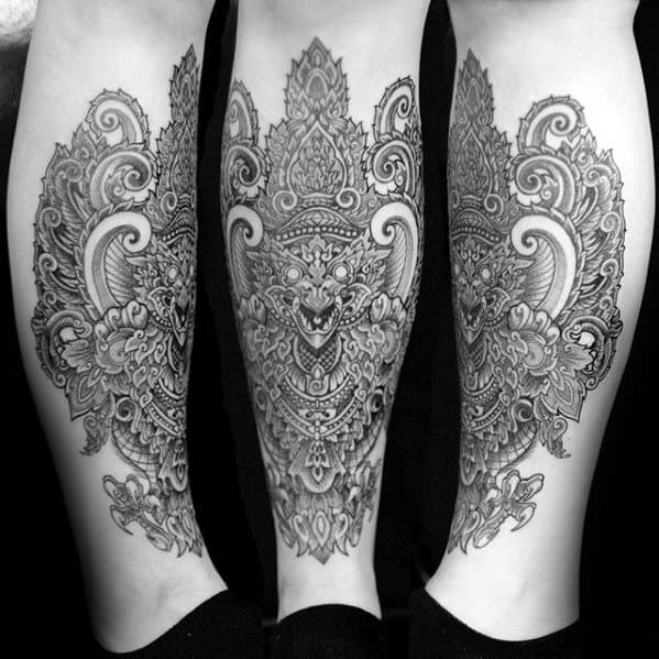 Garuda tattoo on the calf featuring an ornate, symmetrical design with intricate detailing, floral patterns, and a fierce central face.