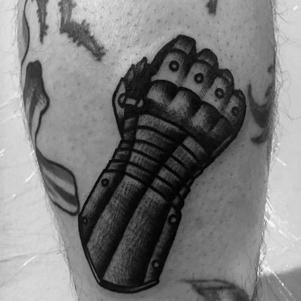 Bold blackwork tattoo of a medieval armored gauntlet in a clenched fist position, with heavy shading and rivet detailing.