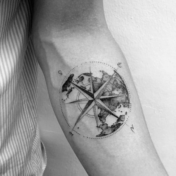 Forearm tattoo of a shaded world map within a detailed compass circle, blending global and directional elements in a fine line style.