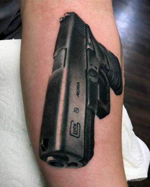 Realistic black and grey tattoo of a Glock 19 on the forearm, featuring detailed shading and perspective for a bold three-dimensional effect.