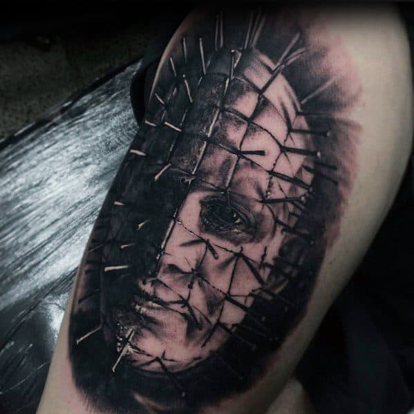 Black and grey *Hellraiser* tattoo of Pinhead with a distorted, eerie expression, deep shading, and intricate pin details for a haunting effect.