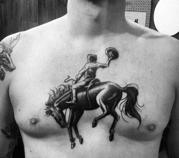 Black and grey chest tattoo of a rodeo cowboy riding a bucking horse, with dynamic pose and detailed linework