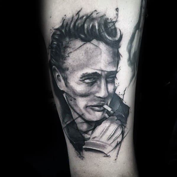Watercolor-style black and grey tattoo of James Dean with a cigarette, featuring artistic ink splatters and expressive shading.
