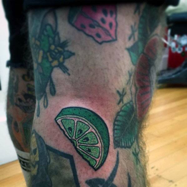 Bold lime wedge tattoo with vibrant green shading and thick black outlines, complementing a colorful, eclectic tattoo collection.