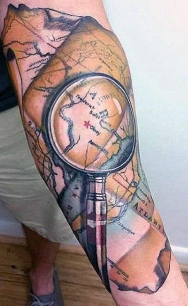 Tattoo of a magnifying glass highlighting a spot on a vintage world map, designed with realistic shading and warm tones for a bold travel-inspired look.
