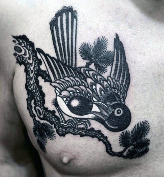 Bold black chest tattoo featuring a stylized magpie with intricate patterns, perched on a branch with pine needles, blending traditional and modern elements.