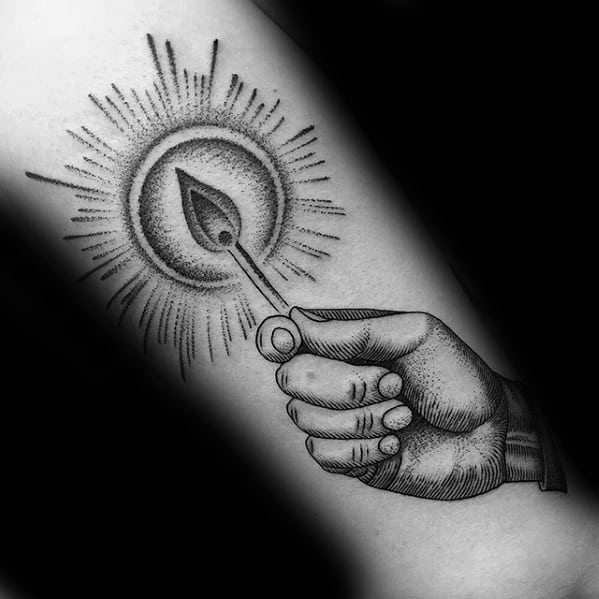 Detailed blackwork tattoo of a hand holding a lit match with radiant light, symbolizing enlightenment, creation, or the start of something new.