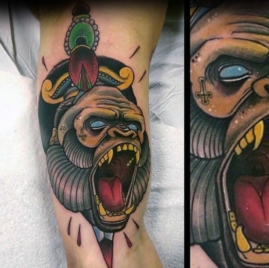 Neo-traditional gorilla tattoo with a golden crown, blank white eyes, open mouth, and vibrant ornamental headpiece.