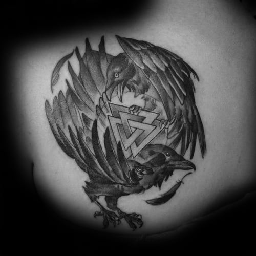 Realistic black and grey tattoo of Huginn and Muninn circling the Valknut symbol, symbolizing Odin’s wisdom and power.