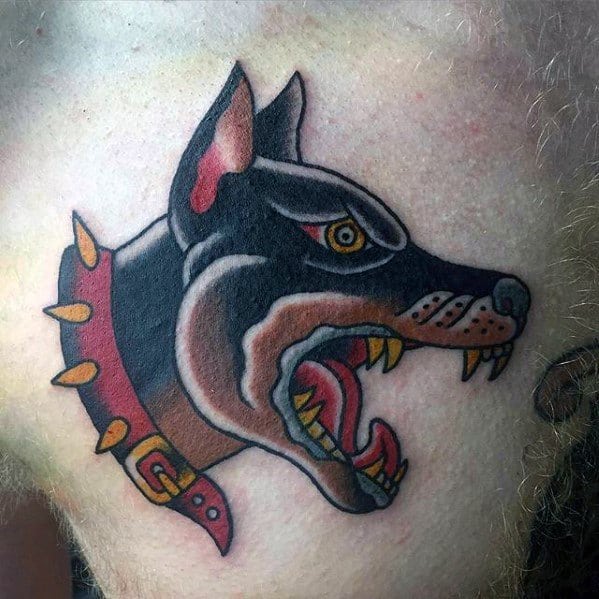 Traditional-style Doberman tattoo with bold outlines, aggressive expression, and vibrant red and yellow tones on a spiked collar.