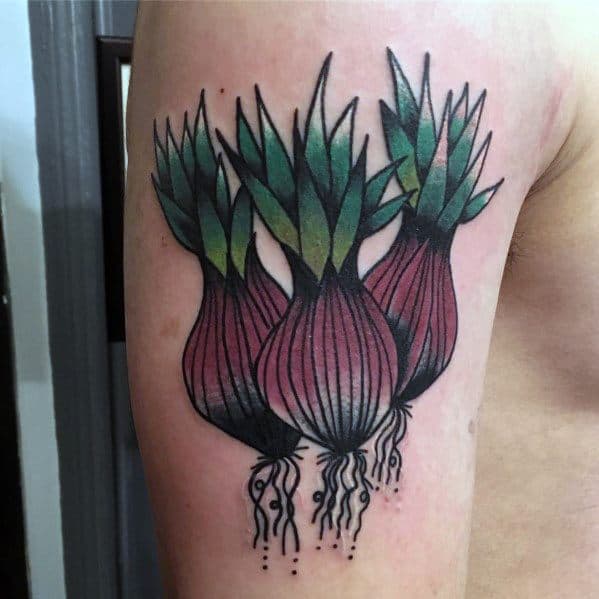 Colorful tattoo of three onions with green leaves and detailed roots on the upper arm, featuring bold outlines and a modern botanical style.