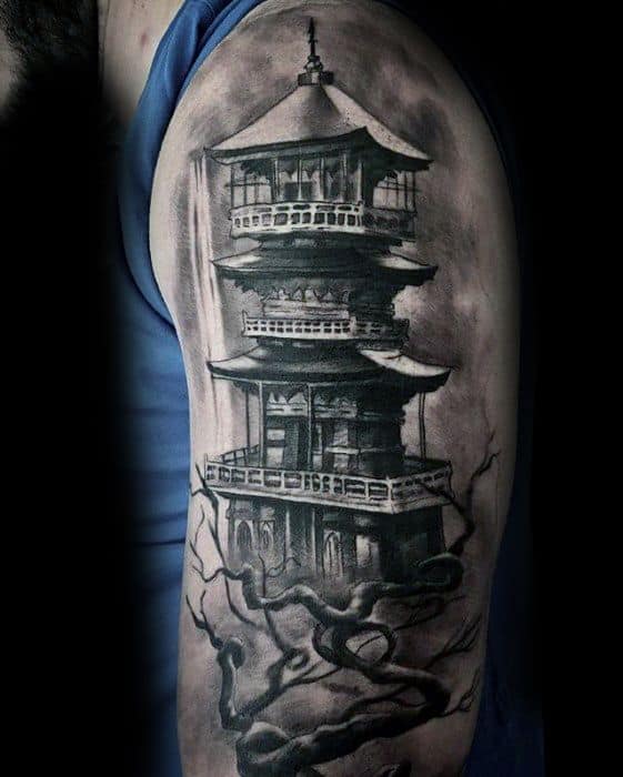 Realistic black and grey upper arm tattoo of a Japanese pagoda with twisted tree branches and a misty, dramatic background.
