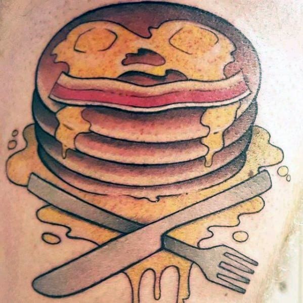 Stack of pancakes tattoo with syrup, butter, bacon, and crossed fork and knife, featuring a bold, vintage-inspired design with warm tones.