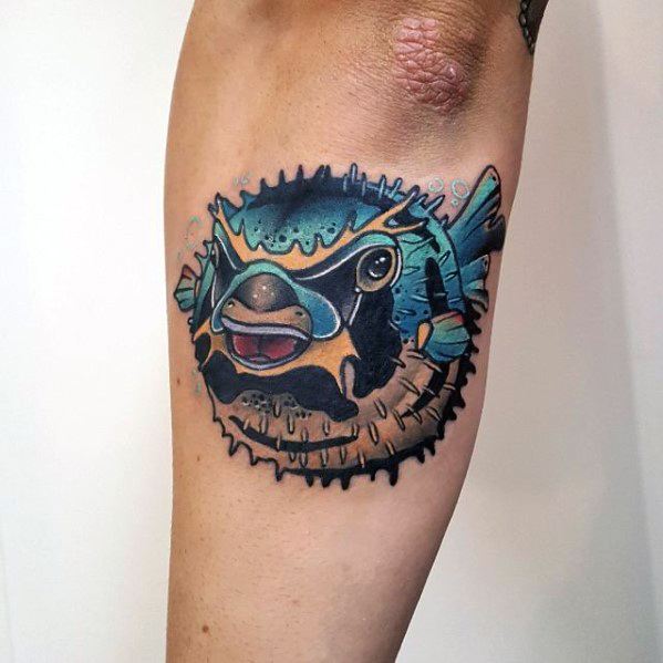 Vibrant pufferfish tattoo with bold shading, rich blue and yellow hues, and a dynamic expression, creating a striking underwater effect.