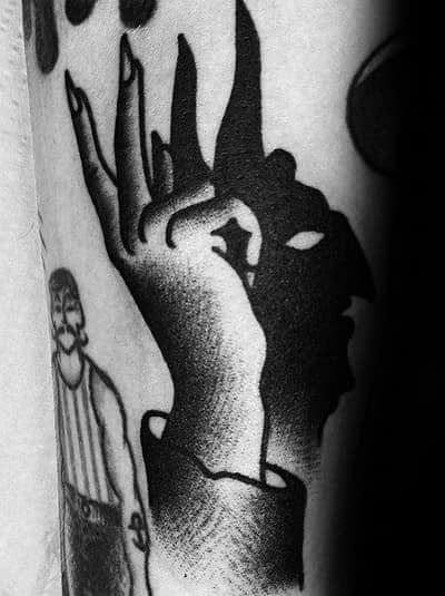 Creative blackwork tattoo of a hand casting a shadow puppet that forms a mysterious face, blending illusion and storytelling.