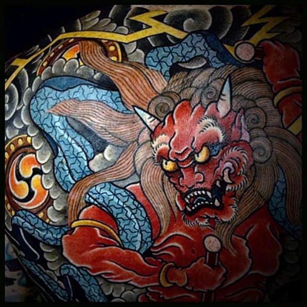 Vibrant Raijin tattoo with fiery red thunder god, wild hair, lightning bolts, and swirling blue ribbons in bold Japanese tradition.