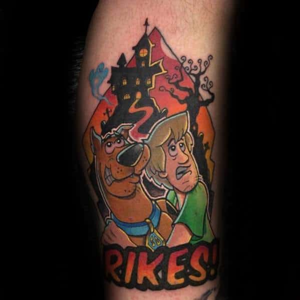 Tattoo of Scooby-Doo and Shaggy looking scared in front of a haunted house with the word “Rikes!” in bold letters below.