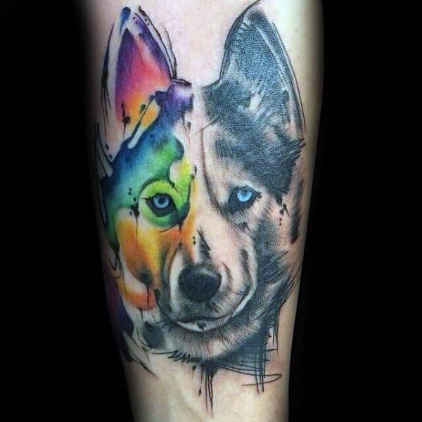 Half-realistic, half-watercolor Siberian Husky tattoo on a man's leg, featuring bold black shading on one side and vibrant rainbow hues on the other.