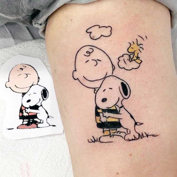 Colorful tattoo of Charlie Brown hugging Snoopy, with Woodstock sitting on Snoopy's head, surrounded by a small cloud, placed on a leg.