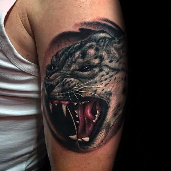 Realistic snow leopard tattoo on the upper arm, capturing a roaring snarl with lifelike shading, sharp teeth, and intense detail.