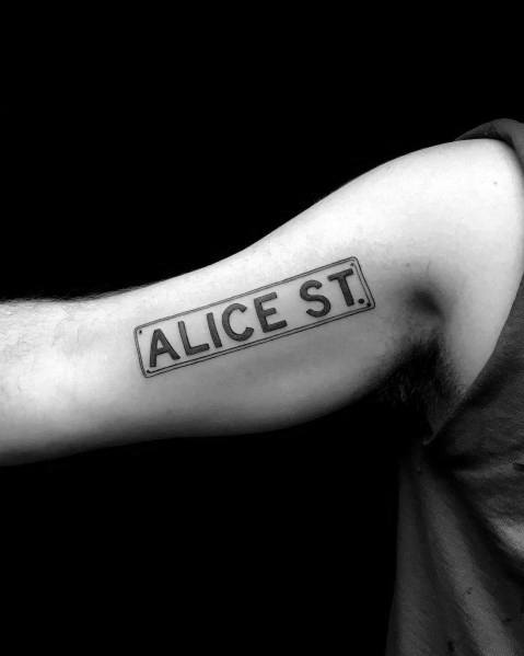 Minimalist black ink tattoo of a rectangular 'Alice St.' street sign, placed on the inner bicep with clean lines and a simple design.