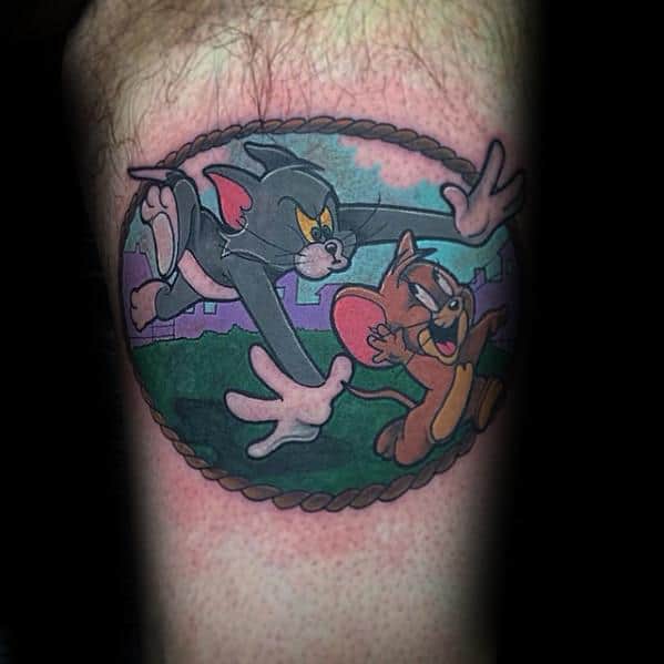 Colorful tattoo of Tom chasing Jerry inside a rope-framed oval, with a cartoon landscape background and dynamic motion.