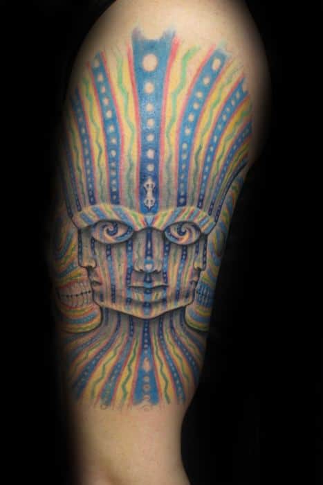 Colorful Tool-inspired upper arm tattoo of a symmetrical face with radiating rainbow lines and glowing blue dots in a psychedelic style.