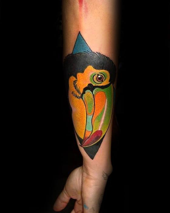 Colorful toucan head tattoo on the forearm with a bold geometric background, featuring vivid yellow, green, and orange tones.
