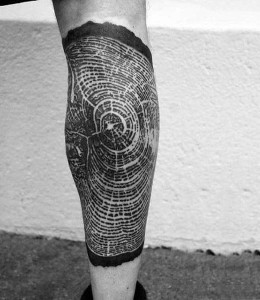 Black ink tree ring tattoo on the calf, featuring intricate growth rings and cracks for a detailed, nature-inspired, and symbolic design.