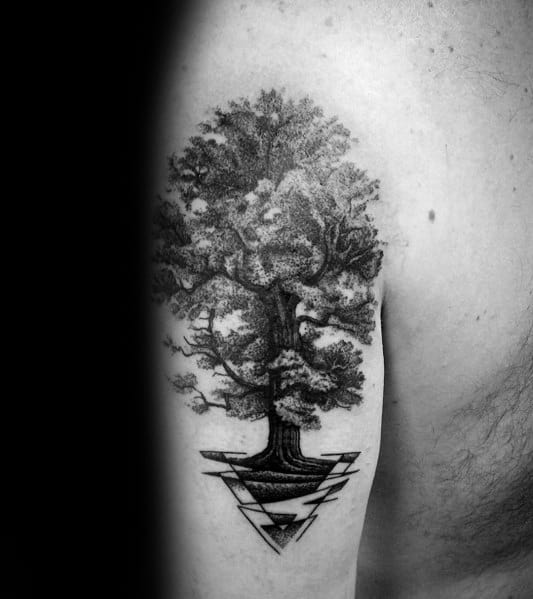 Black and grey upper arm tattoo of a detailed tree with lush foliage, growing from a geometric design, symbolizing strength and balance.