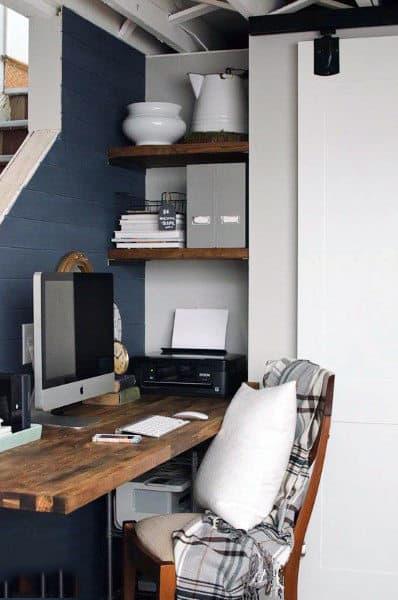 Cozy home office with a wooden desk, computer, printer, and shelves with decor and books; a blanket draped over the chair