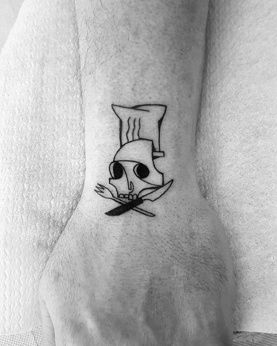 Minimalist black line tattoo of a skull wearing a chef's hat, with a crossed fork and knife below, placed on the inner ankle.