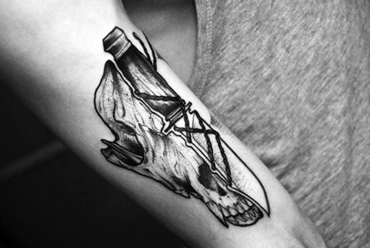 Tattoo of a wolf skull intricately intertwined with a bottle and geometric designs on a forearm