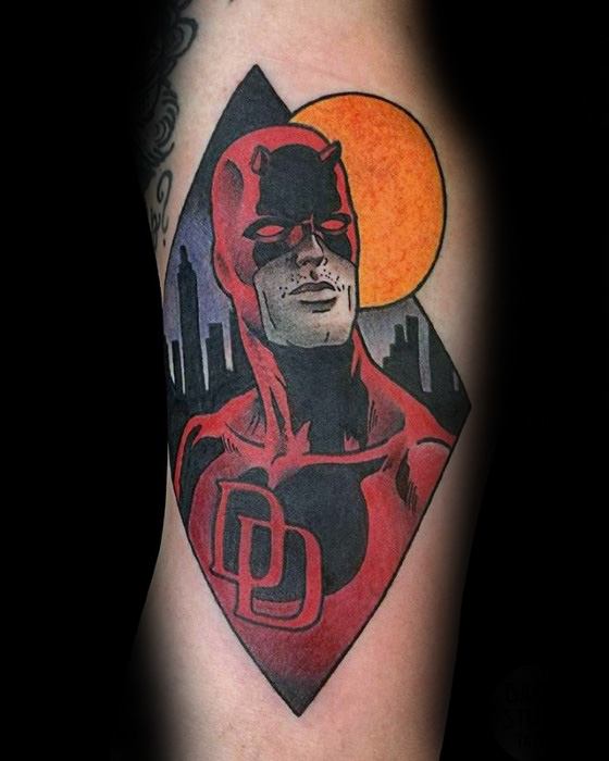 Stylized Daredevil tattoo inside a diamond frame with bold red tones, city skyline, and a glowing orange sun in the background.