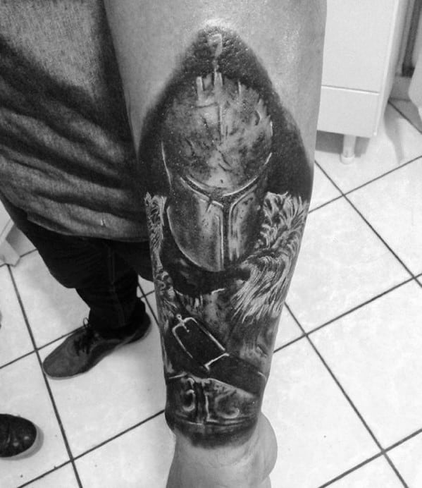 Black and grey Dark Souls tattoo of a knight in worn armor and fur cloak, with dramatic shading on the forearm.