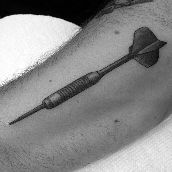 Clean black and grey tattoo of a single dart with detailed shading, placed on the upper arm to reflect precision and focus.
