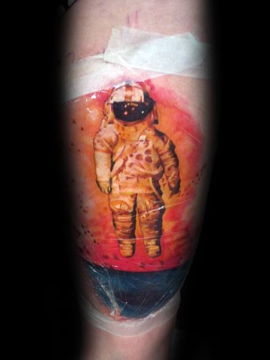 Freshly inked Deja Entendu astronaut tattoo with a vivid red-orange sky, black birds, and a deep blue ocean at the bottom.